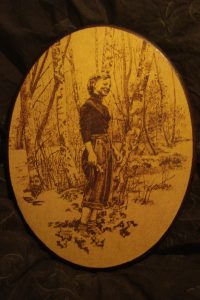 oval glödritad tavla, leende kvinna i björkskog med en bukett vitsippor i handen